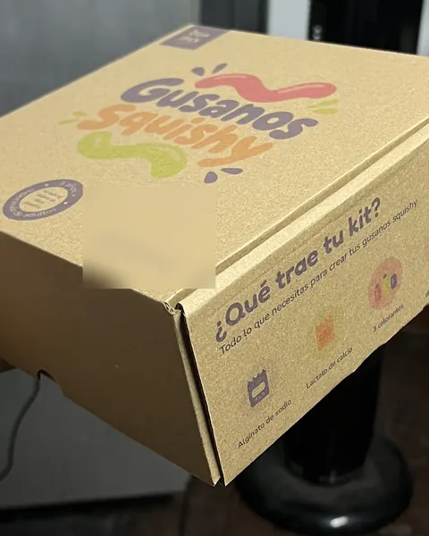 Caja de envío kraft de un kit infantil con el logo a color y el costado impreso con lo que trae el kit