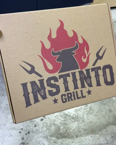 Caja de envío kraft cerrada con el logo de un restaurante de parrillas impreso en rojo y negro